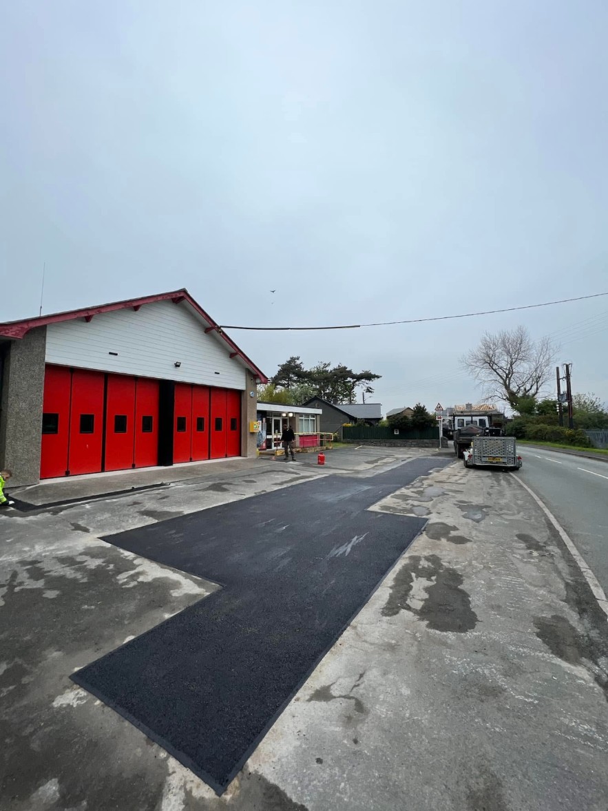 Fresh tarmac repair outside a commercial building with red doors
